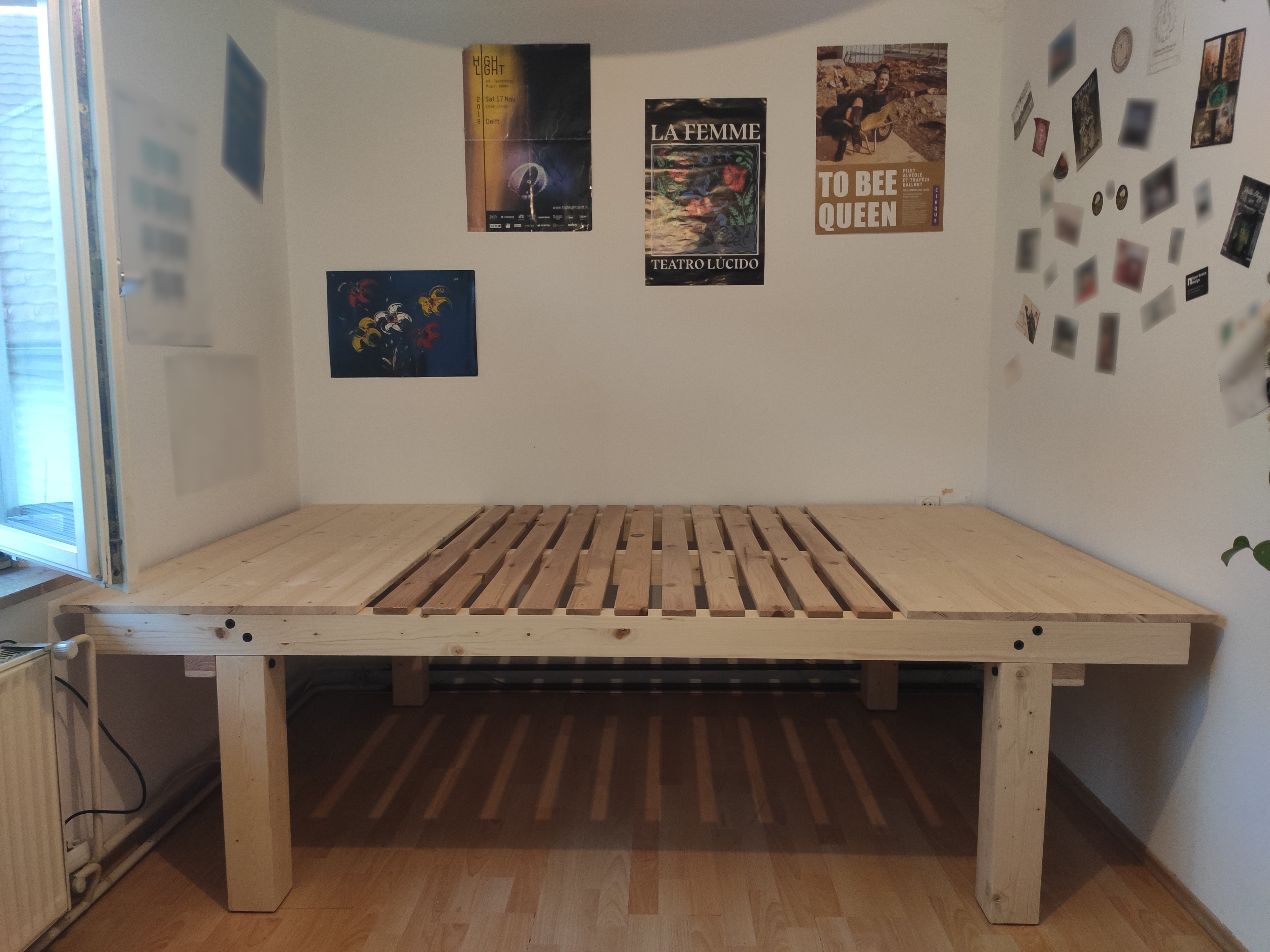 a DIY bed frame made out of wood in a small room, spanning from wall to wall.